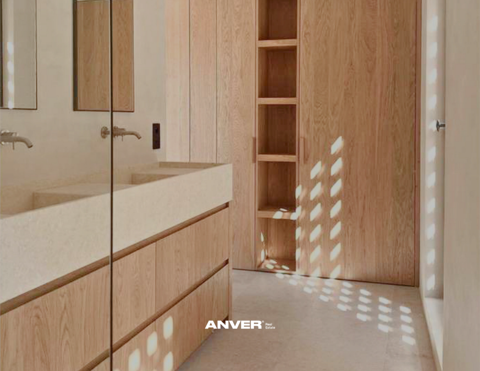 Vista interior de un baño con pared de madera, lavabo de cerámica, espejo y estantes abiertos de madera, con luz que crea patrones de sombra en la pared.