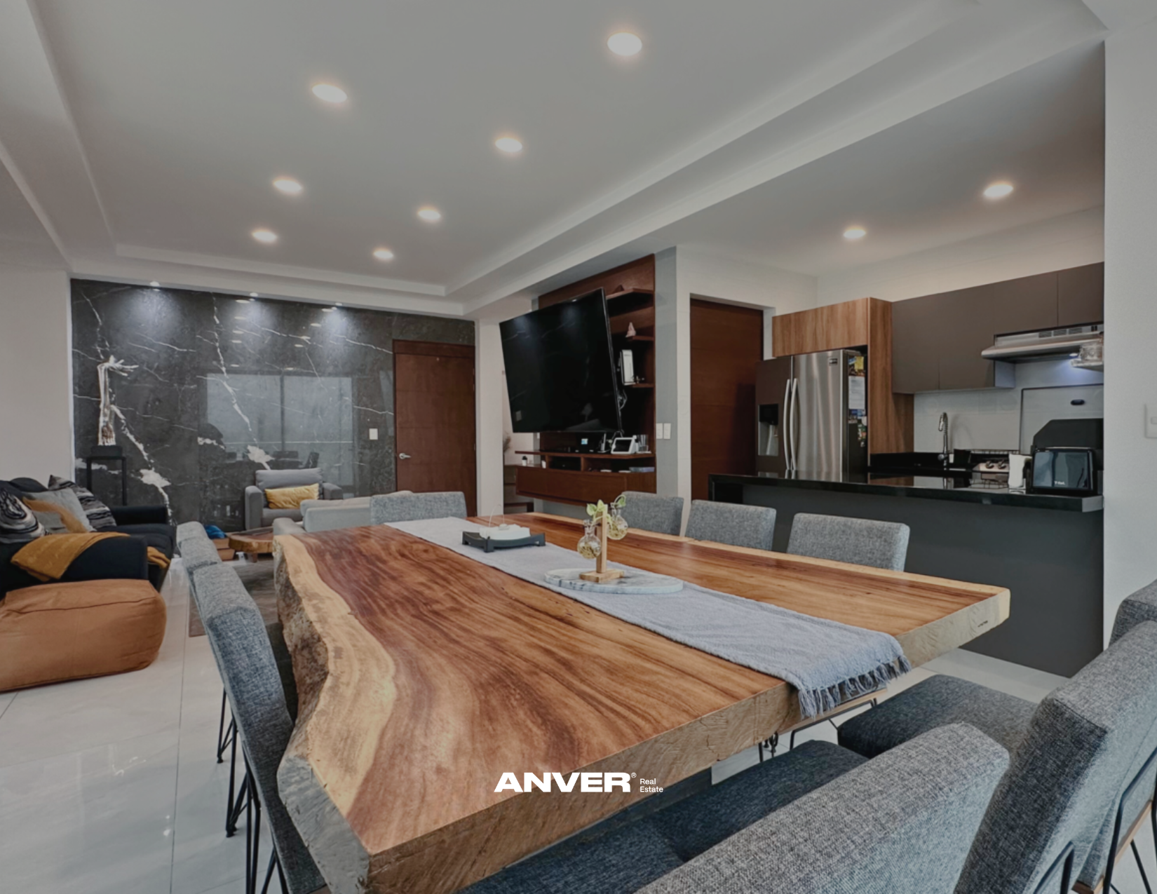 Sala de estar moderna con un comedor de madera, sillones y una cocina en el fondo.