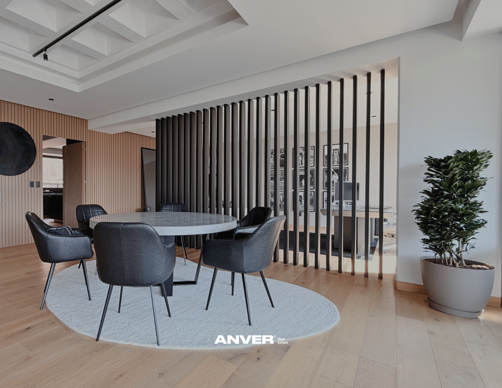 Sala de reuniones con mesa redonda y sillas negras, división de madera y jardineras decorativas en el fondo.