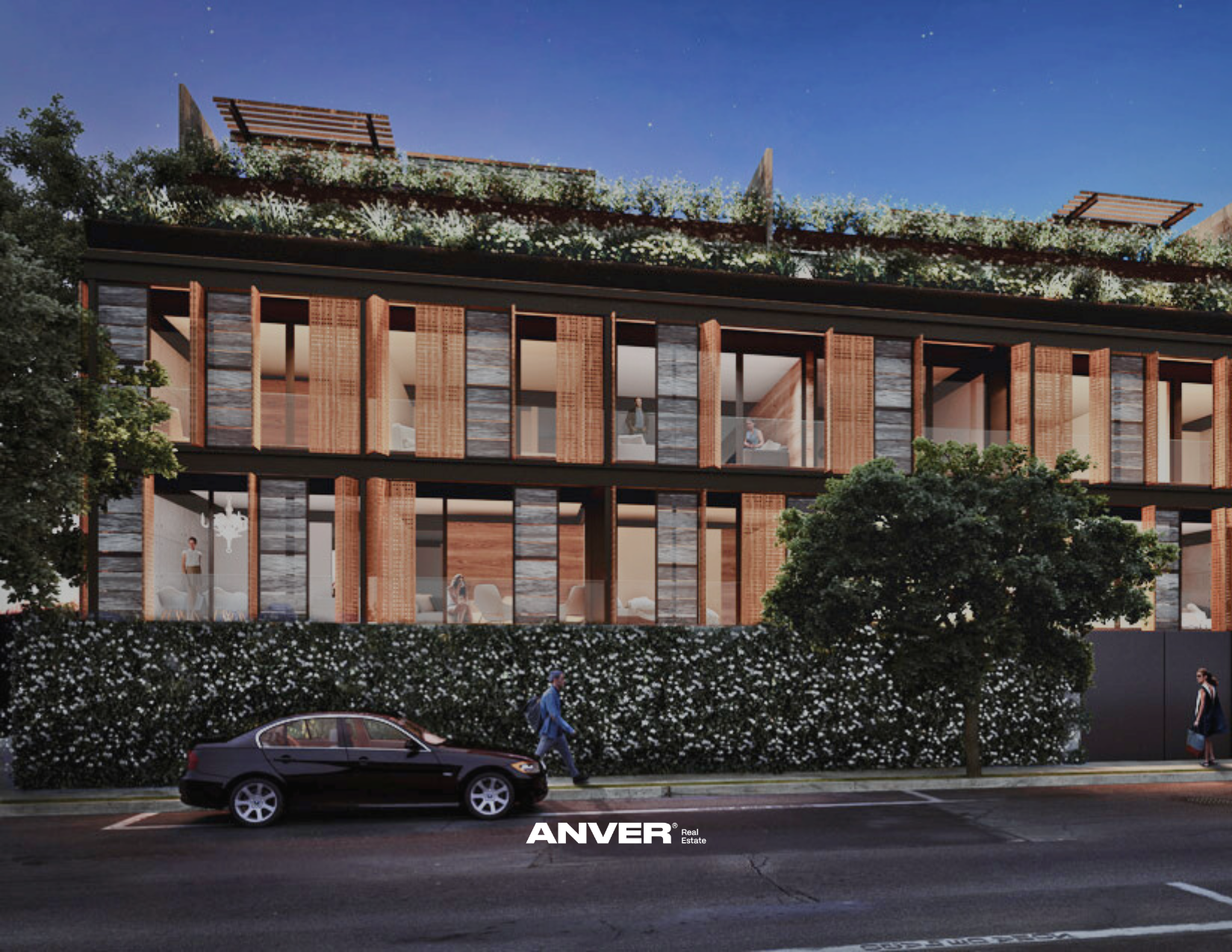 Edificio moderno con grandes ventanas y madera en su fachada, con un techo ajardinado y árboles en el exterior, en la noche.