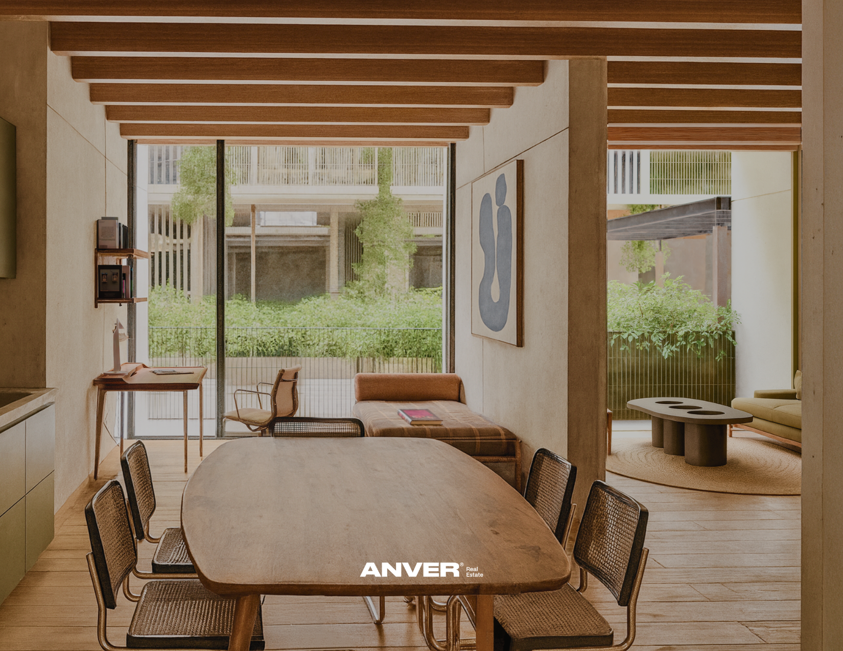 Vista interior de una sala moderna con muebles de madera, ventanas grandes que dejan ver un jardín exterior con árboles verdes, una mesa ovalada con sillas, un sofá naranja con una revista encima, y una decoración minimalista.