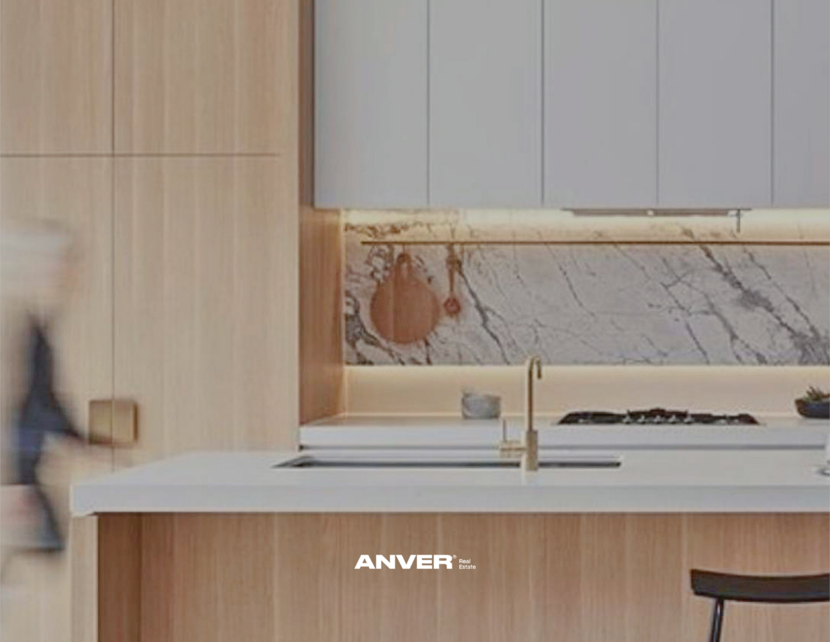 Vista de una cocina moderna con encimera de madera, pared de mármol, fregadero dorado, estufa y armarios grises