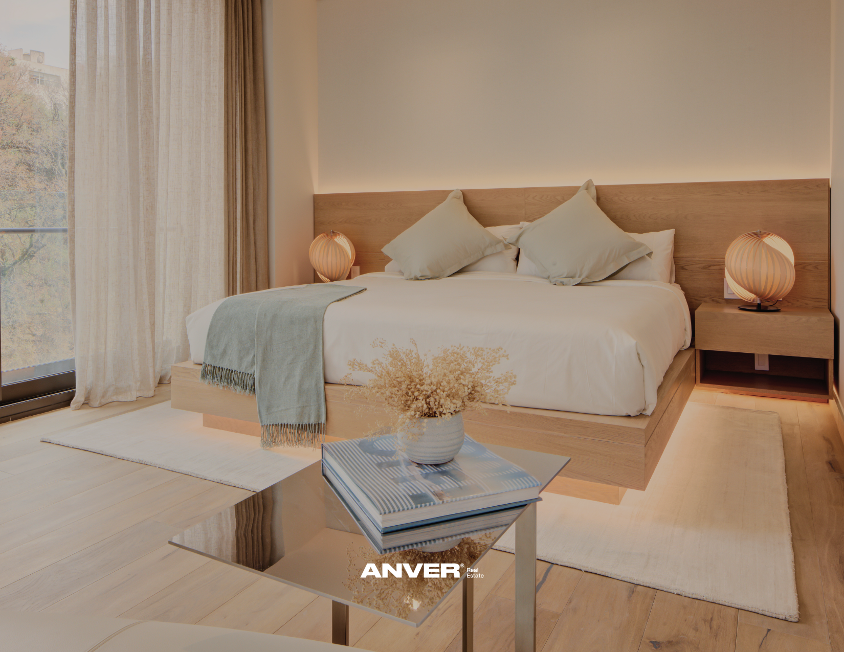 Habitación moderna con cama grande, cortinas claras, lámparas de mesa y mesa auxiliar con libro y florero.