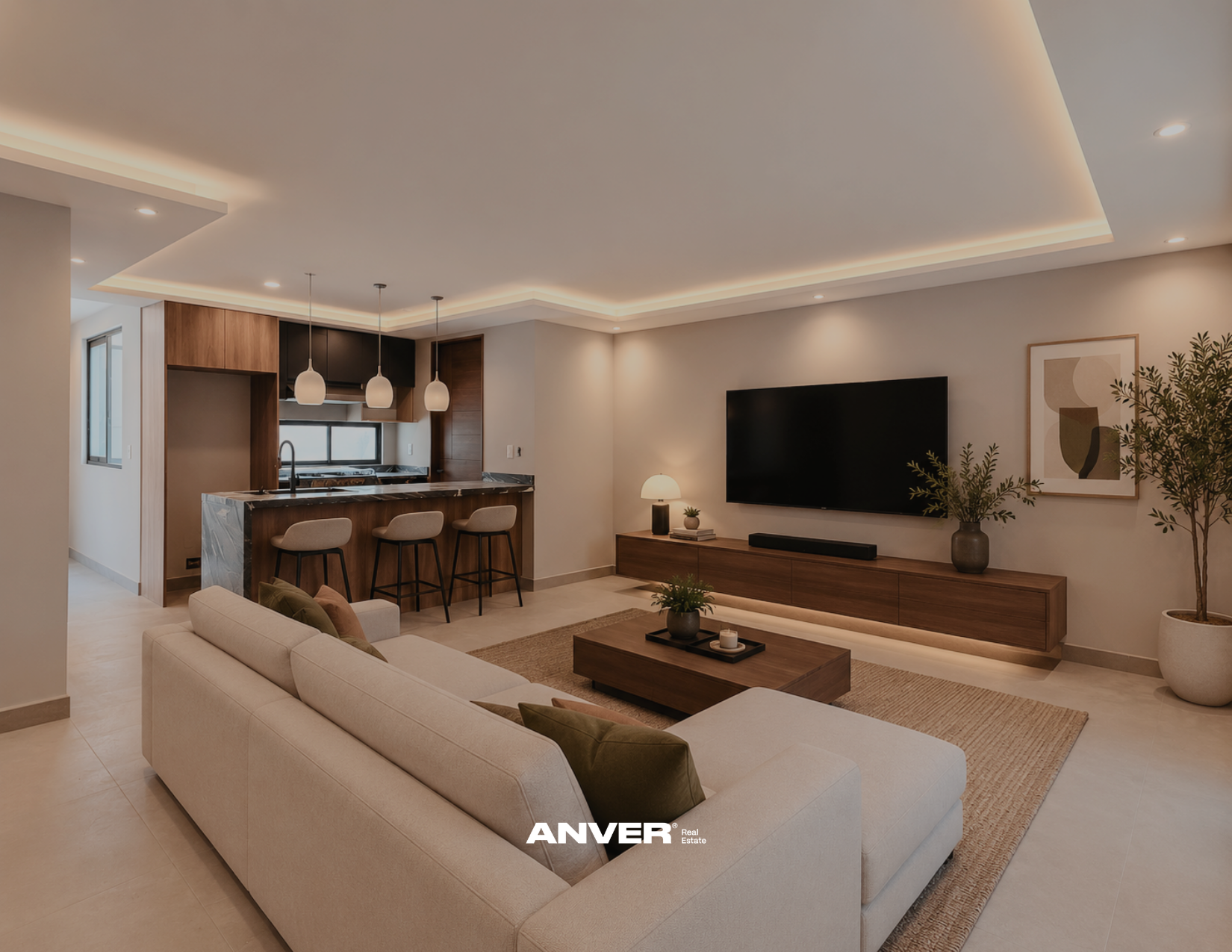 Sala moderna con sofá beige, mesa de centro de madera, televisor grande, mueble de madera, planta y lámpara, vista hacia la cocina con barra de mármol y sillas beige, techo con iluminación empotrada.