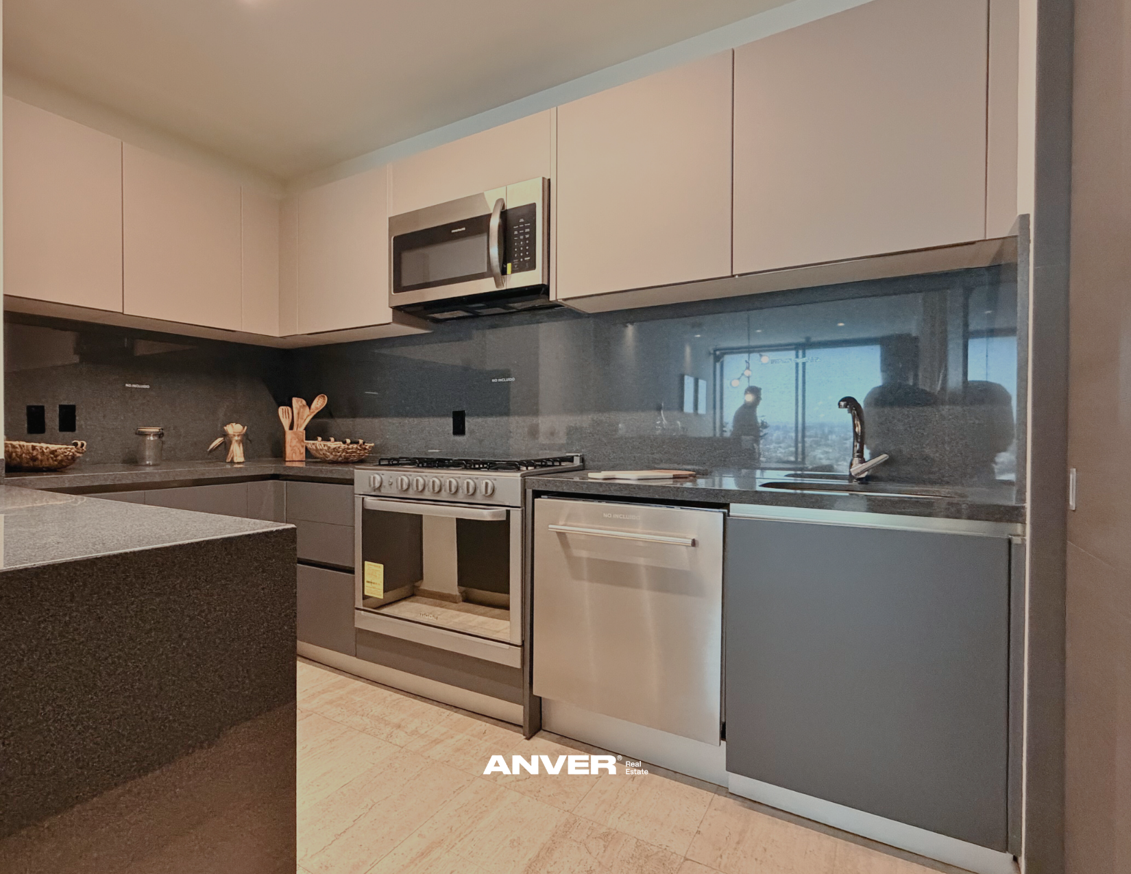 Cocina moderna con gabinetes grises, estufa de horno, microondas y fregadero, con reflejo de personas y vista exterior en la ventana.