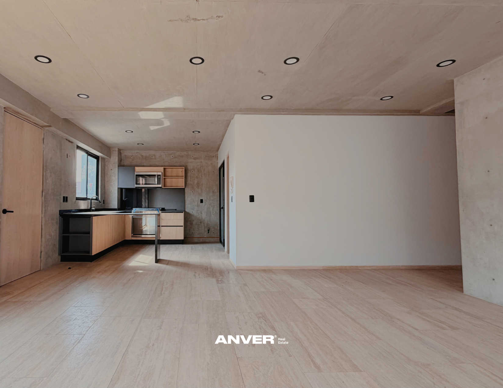 Interiores de casa en construcción, con cocina moderna, paredes blancas y techos de cemento, piso de madera clara, ventanas y puertas sin acabados.