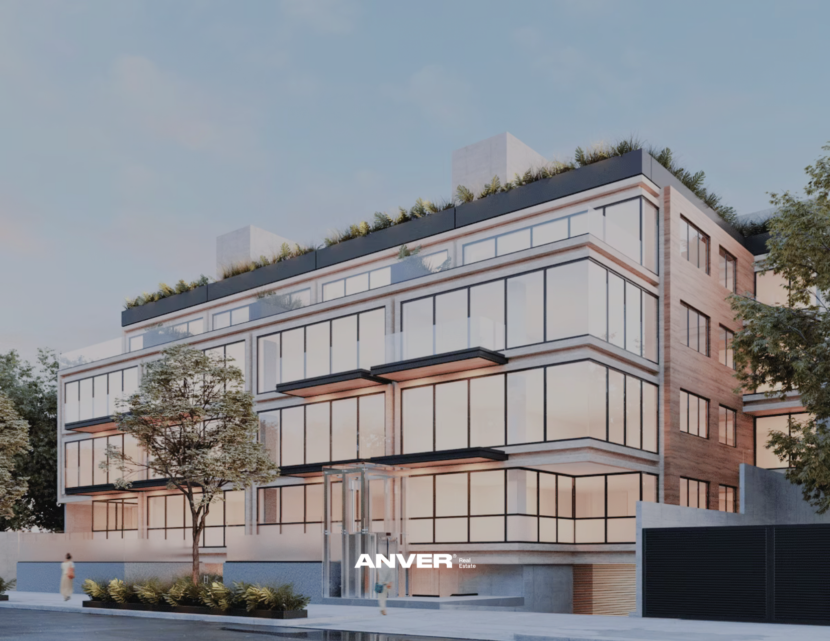 Edificio moderno de varias plantas con grandes ventanales de vidrio, rodeado de árboles y vegetación, con el logo de ANVER Real Estate en la parte inferior.