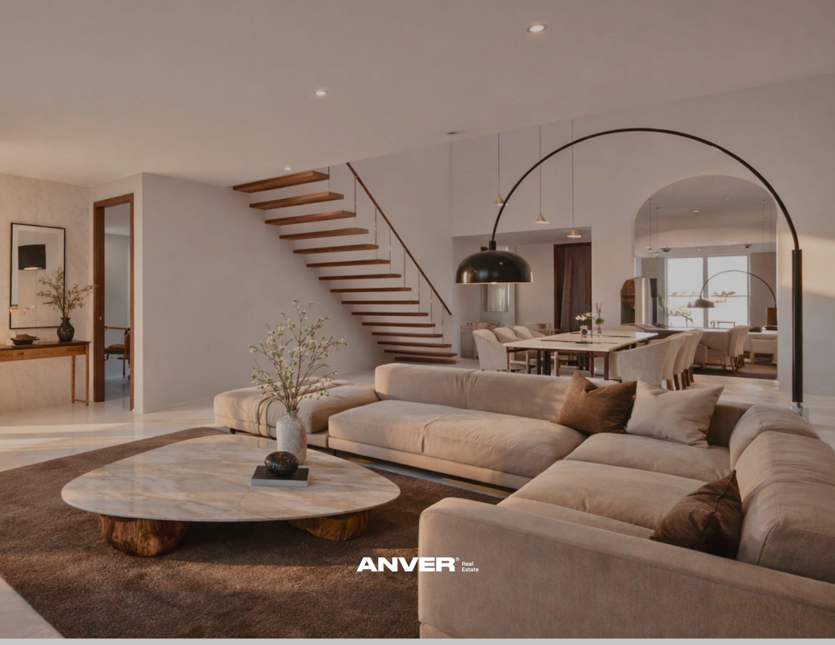Sala de estar moderna con sofá beige, mesa de centro de madera y mármol, plantas decorativas, y escaleras de madera con baranda delgada en una casa bien iluminada.