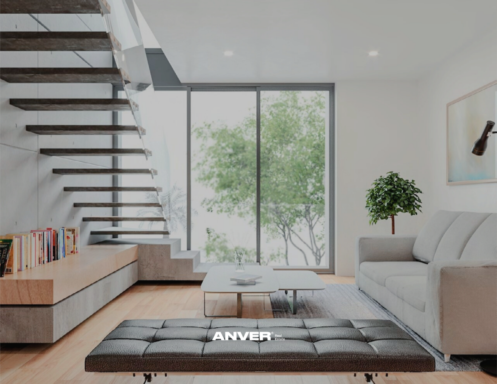 Sala moderna con sofá gris, mesa blanca, planta, estantería con libros, escaleras abiertas y ventanas grandes con vista a árboles verdes.