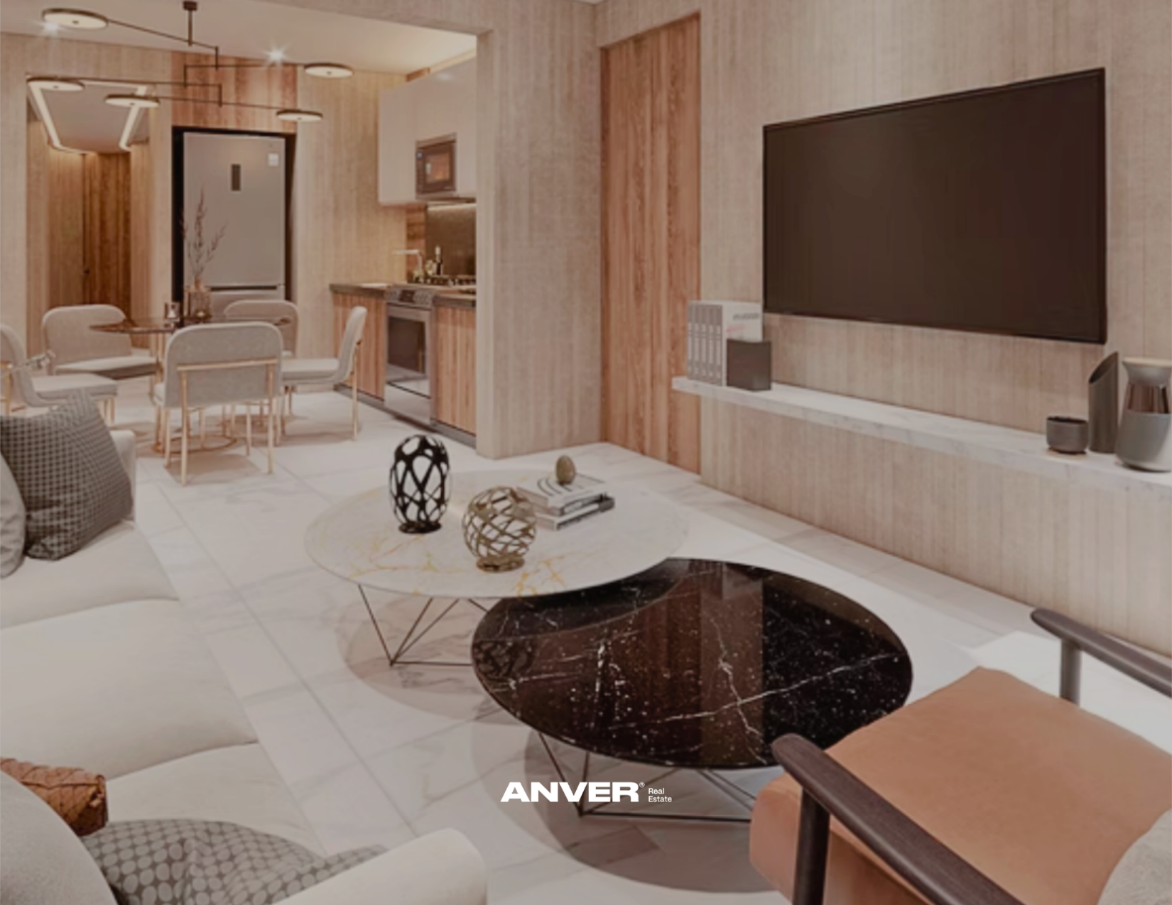 Sala de estar con sofá, mesa central de mármol, decoración moderna, televisión en la pared, cocina de fondo con electrodomésticos y comedor con sillas blancas.