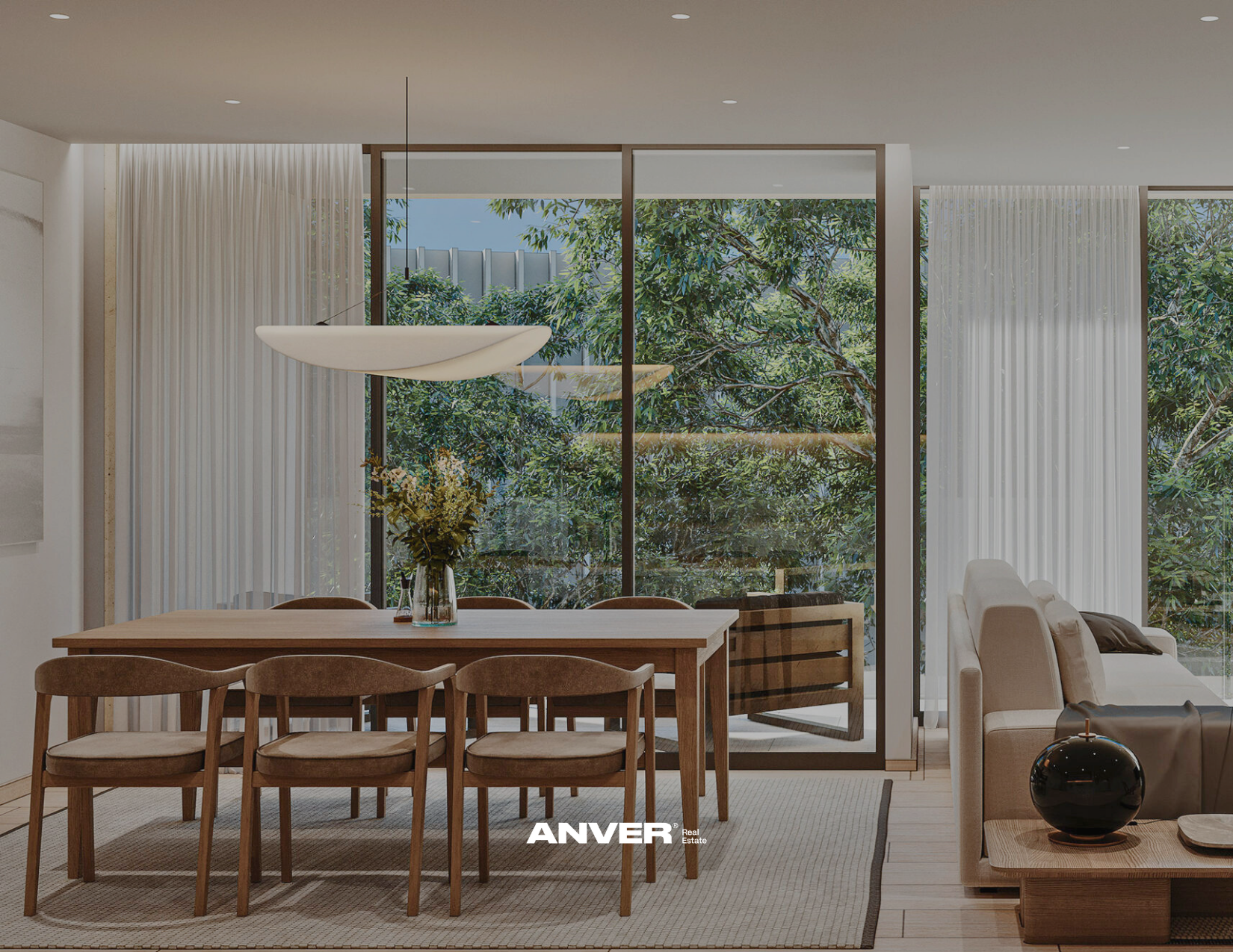 Sala moderna con mesa de madera, siete sillas y una planta en un florero en el centro, grandes ventanas con cortinas blancas, vista a árboles exteriores, sofá blanco y mesa auxiliar con decoración.