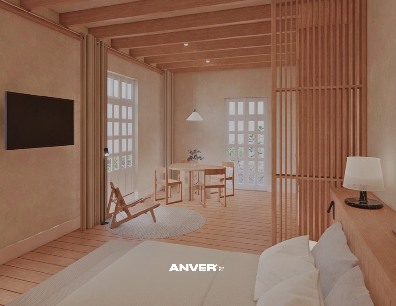 Vista de una sala de estar con paredes y techo de madera, ventanas con cortinas beige, una mesa redonda con cuatro sillas, una lámpara colgante y una televisión montada en la pared. También hay un sofá con cojines y una lámpara de mesa.