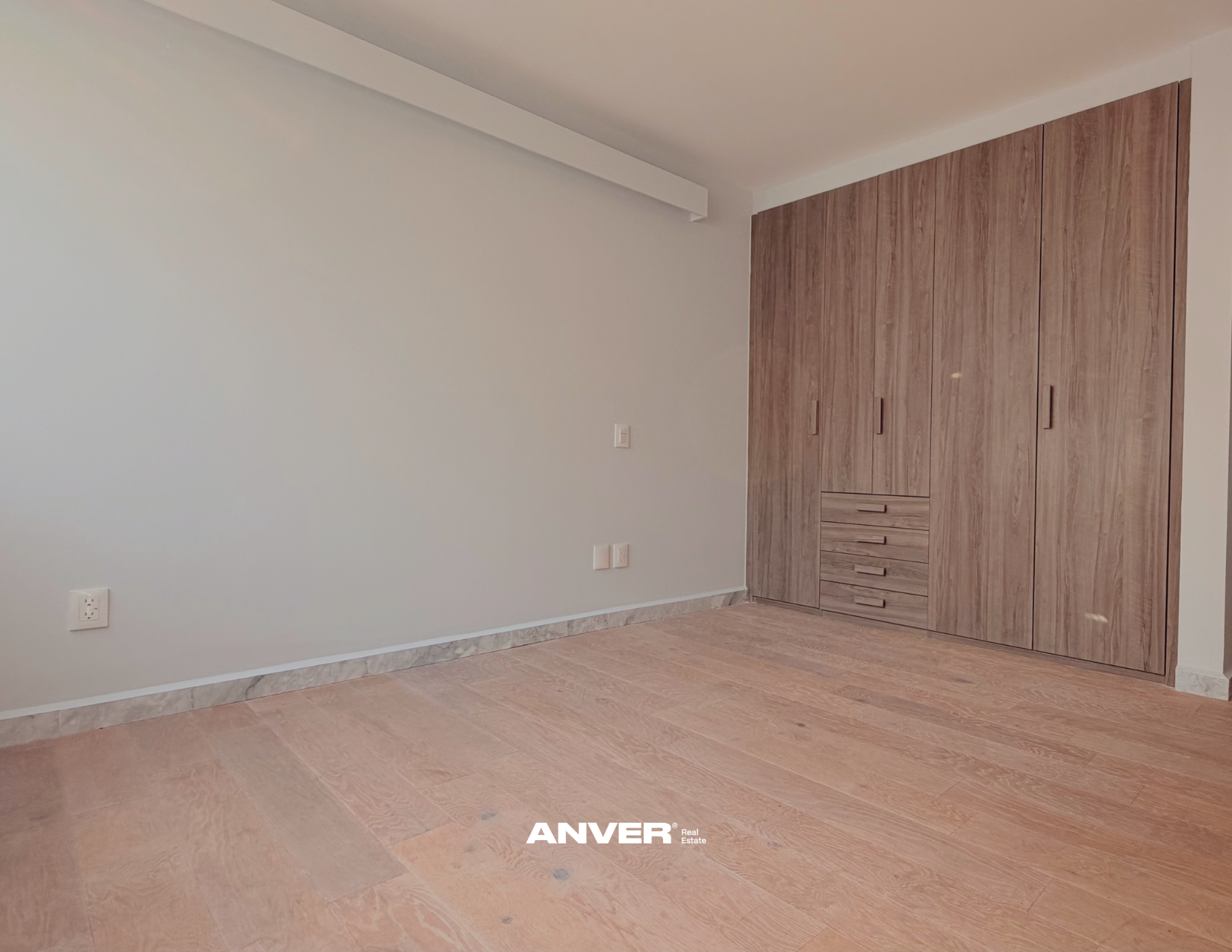 Habitación vacía con paredes blancas, suelo de madera y armario empotrado de madera.