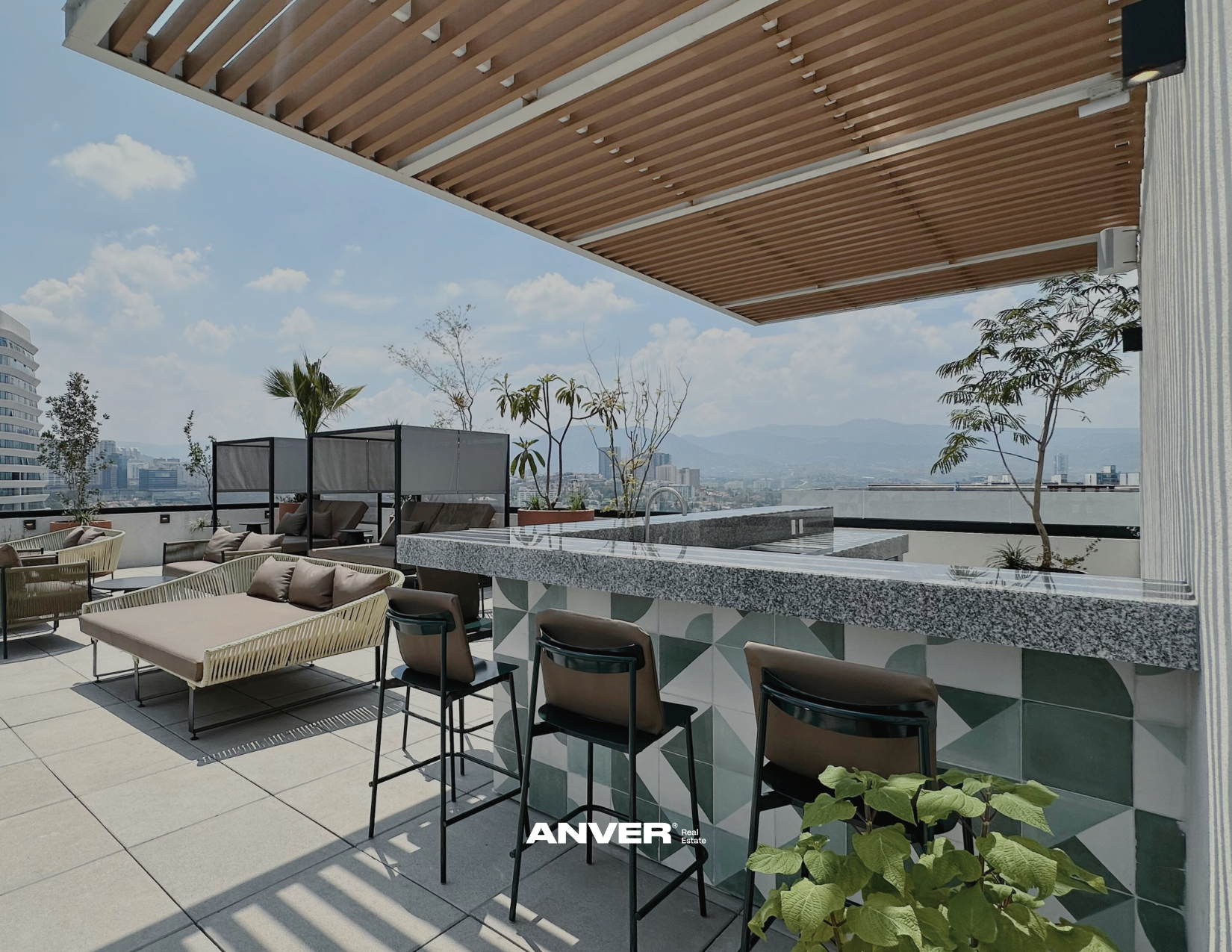 Terraza en la azotea con muebles de descanso, área de bar, plantas y vista de la ciudad y las montañas en el fondo.