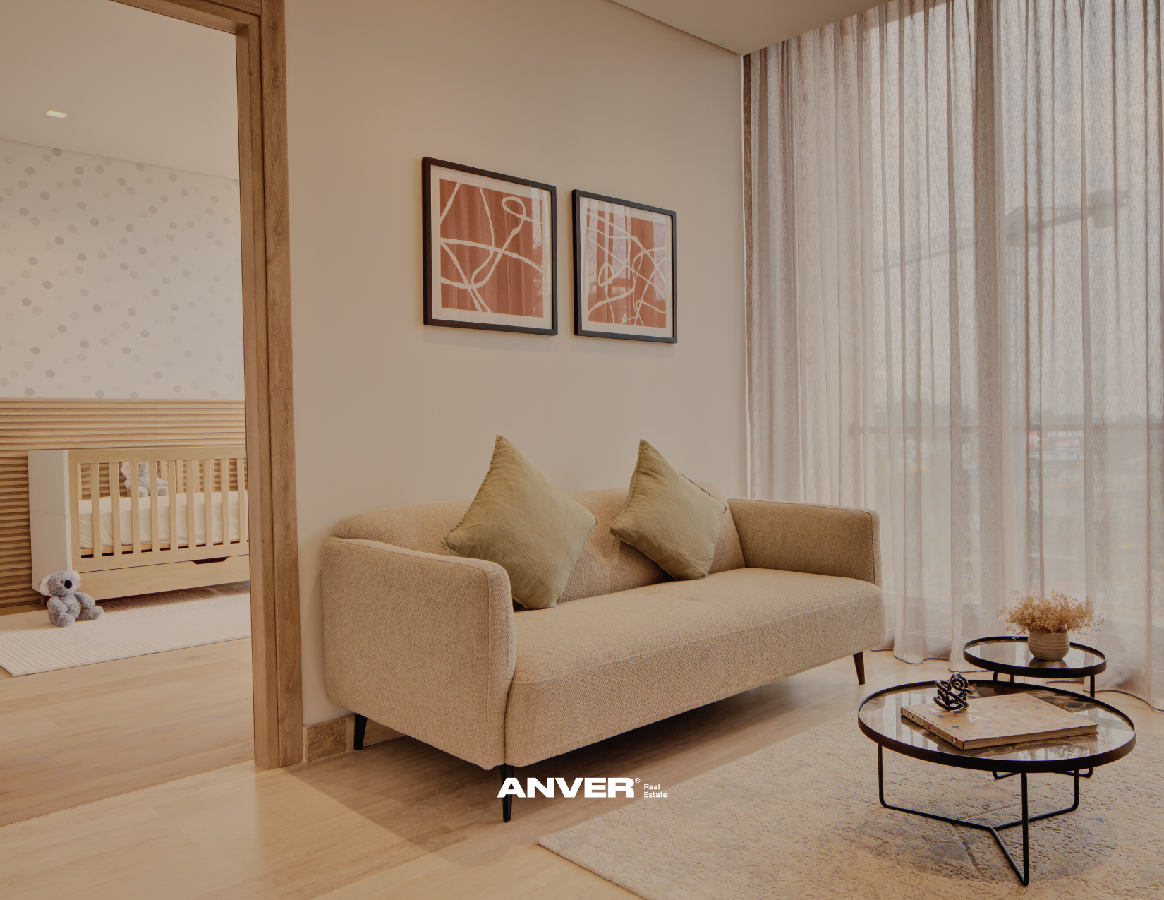 Sala de estar con sillón beige, dos cojines, paredes blancas, cuadros abstractos, cortinas claras y ventanas grandes con vista a la ciudad.