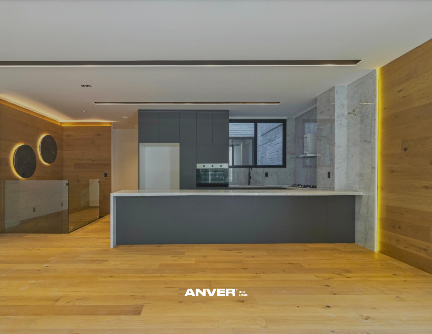 Interiores modernos de cocina con encimera de piedra, pared de madera y ventanas grandes que permiten la entrada de luz natural.