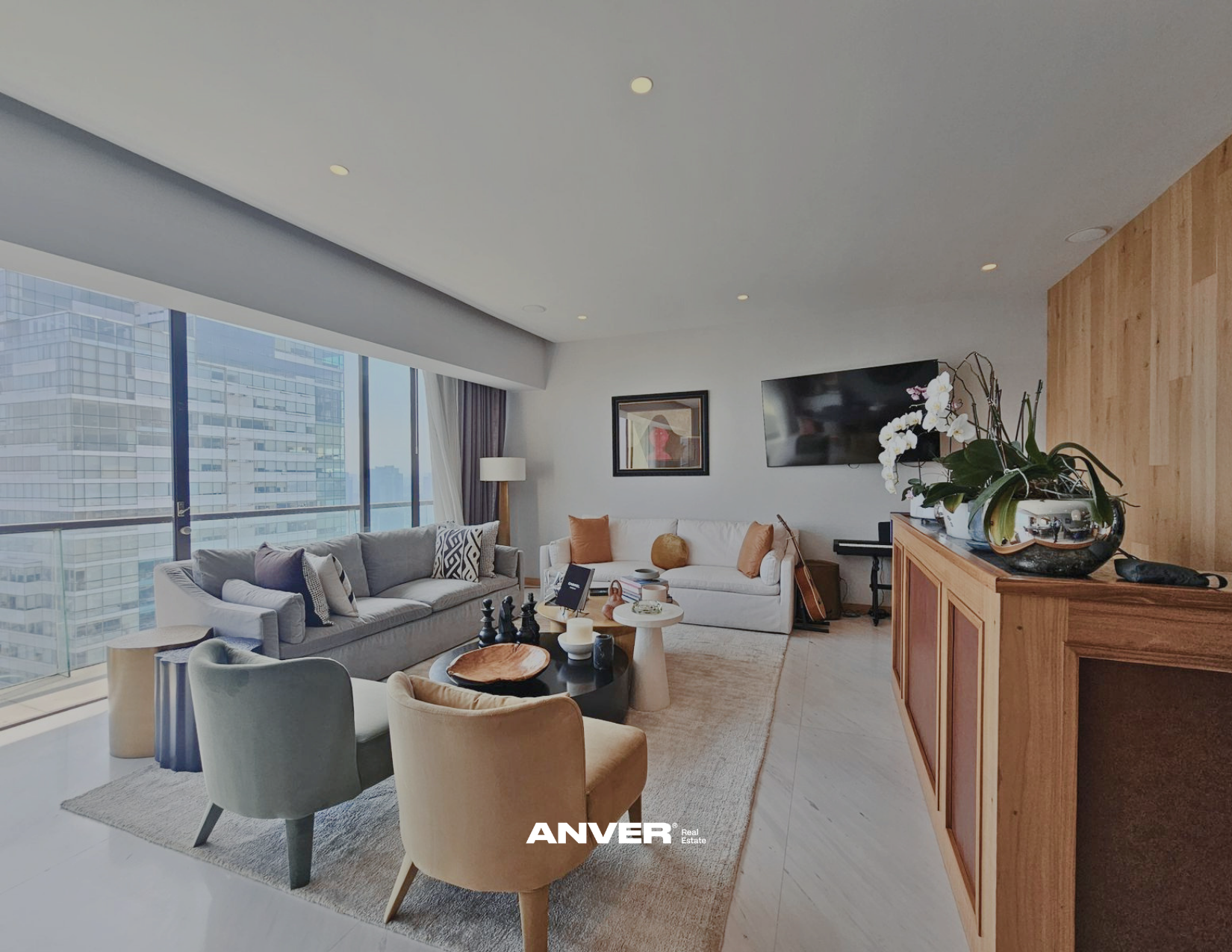 Sala de estar moderna con ventanas de pisos a techo que muestran edificios altos, muebles cómodos en tonos neutros, mesas decorativas y un televisor en la pared. Decoración con plantas y cuadros.