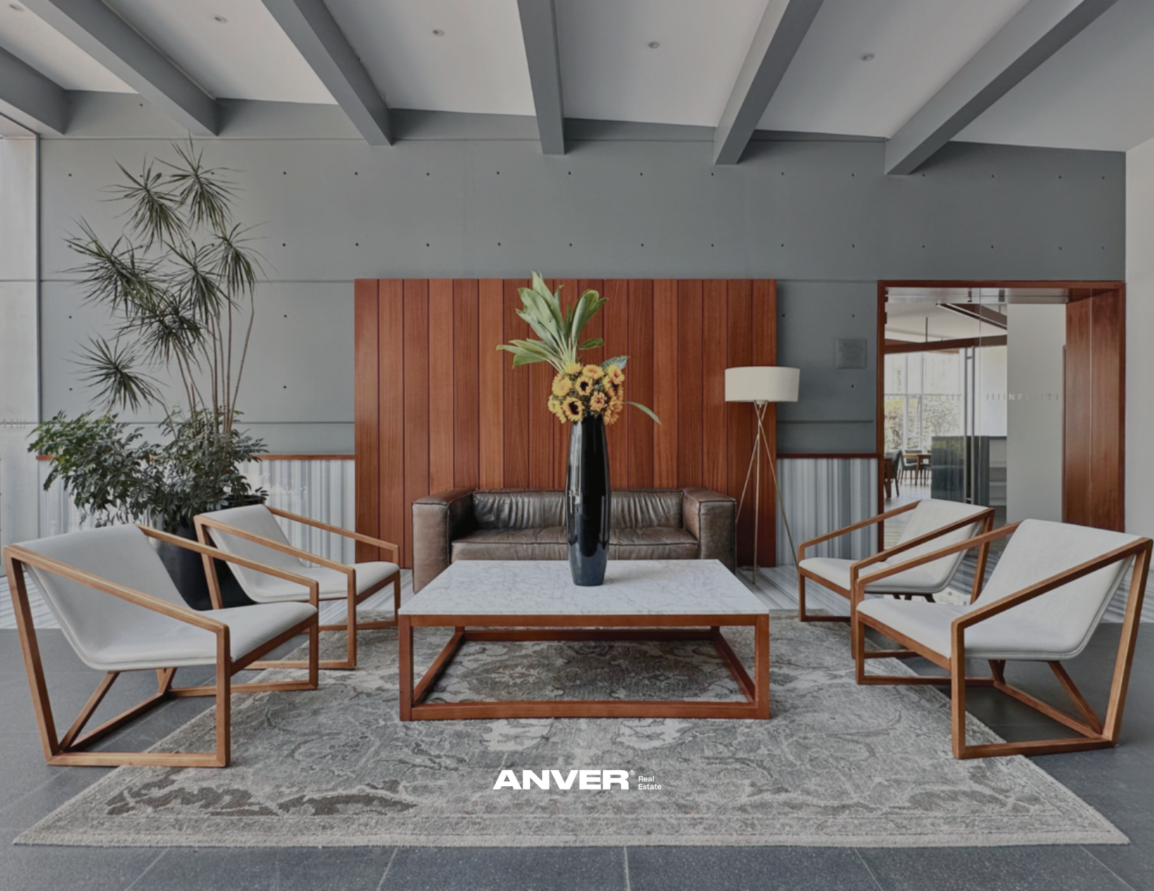 Rincón de sala moderna con sillas de madera y cojines blancos, mesa de centro de madera y mosaico, vaso con flores en el centro, pared de madera y plantas de interior, alfombra gris y lámpara de pie.