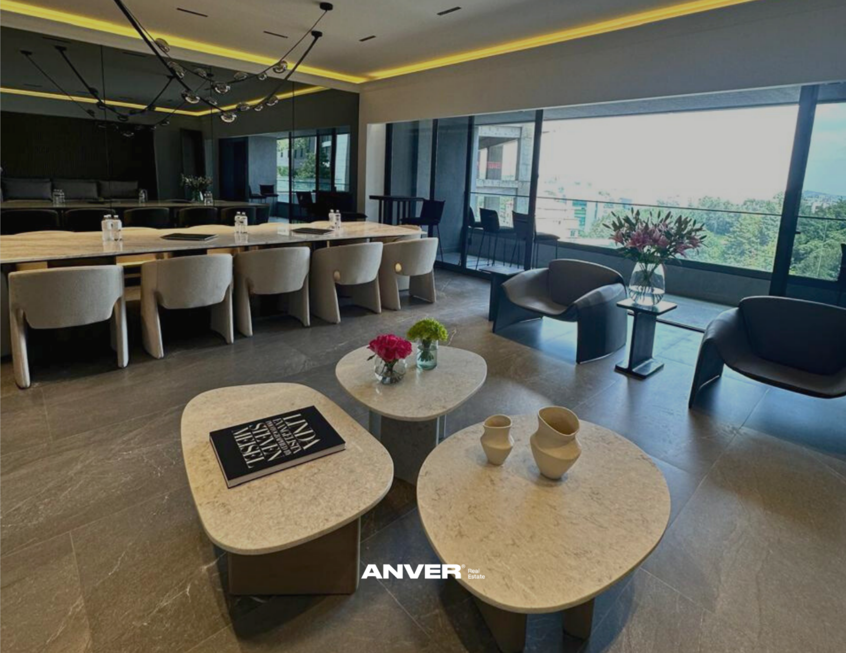 Sala de reuniones moderna con mesas de mármol, sillas cómodas y ventanas grandes que dejan entrar mucha luz natural, decorada con flores en jarrones y objetos decorativos.