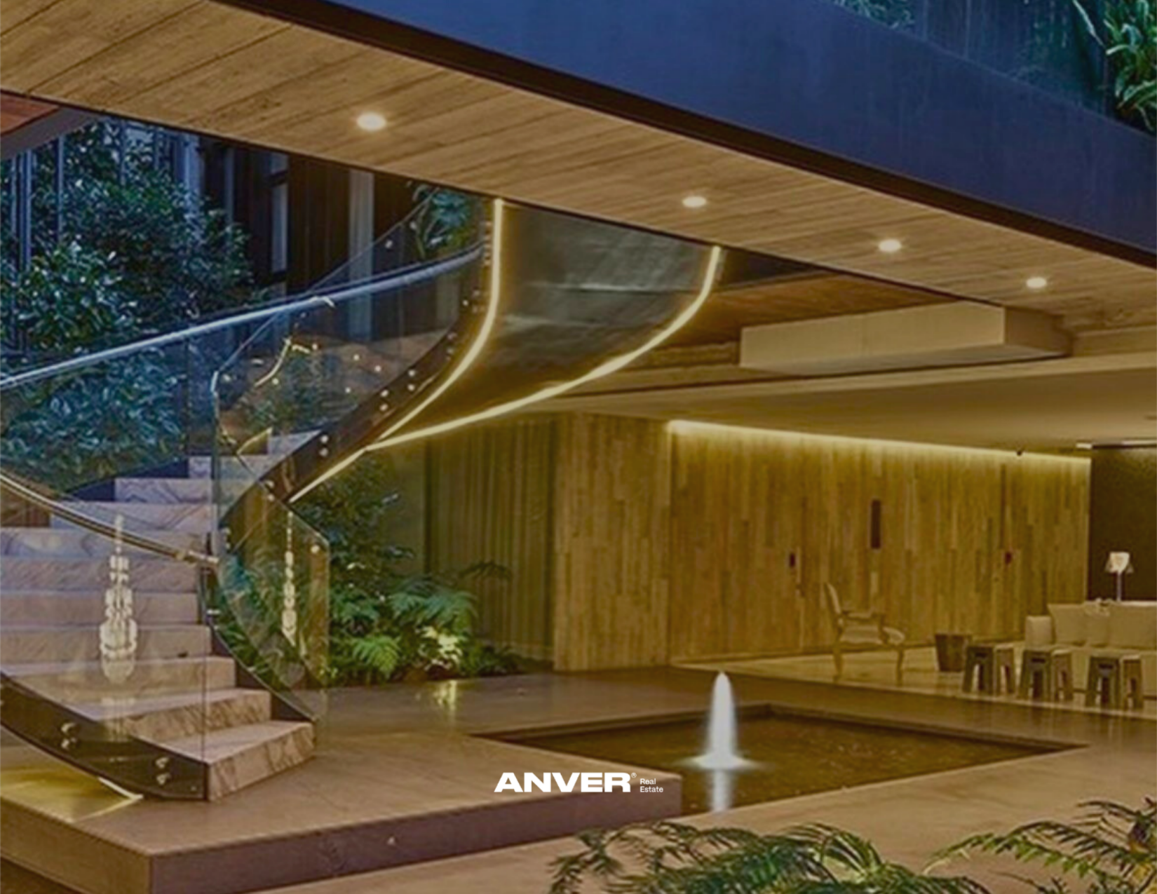 Interior moderno con escaleras de cristal, madera y iluminación LED, área social con zona de comedor y fuente en el centro, decorado con plantas tropicales.