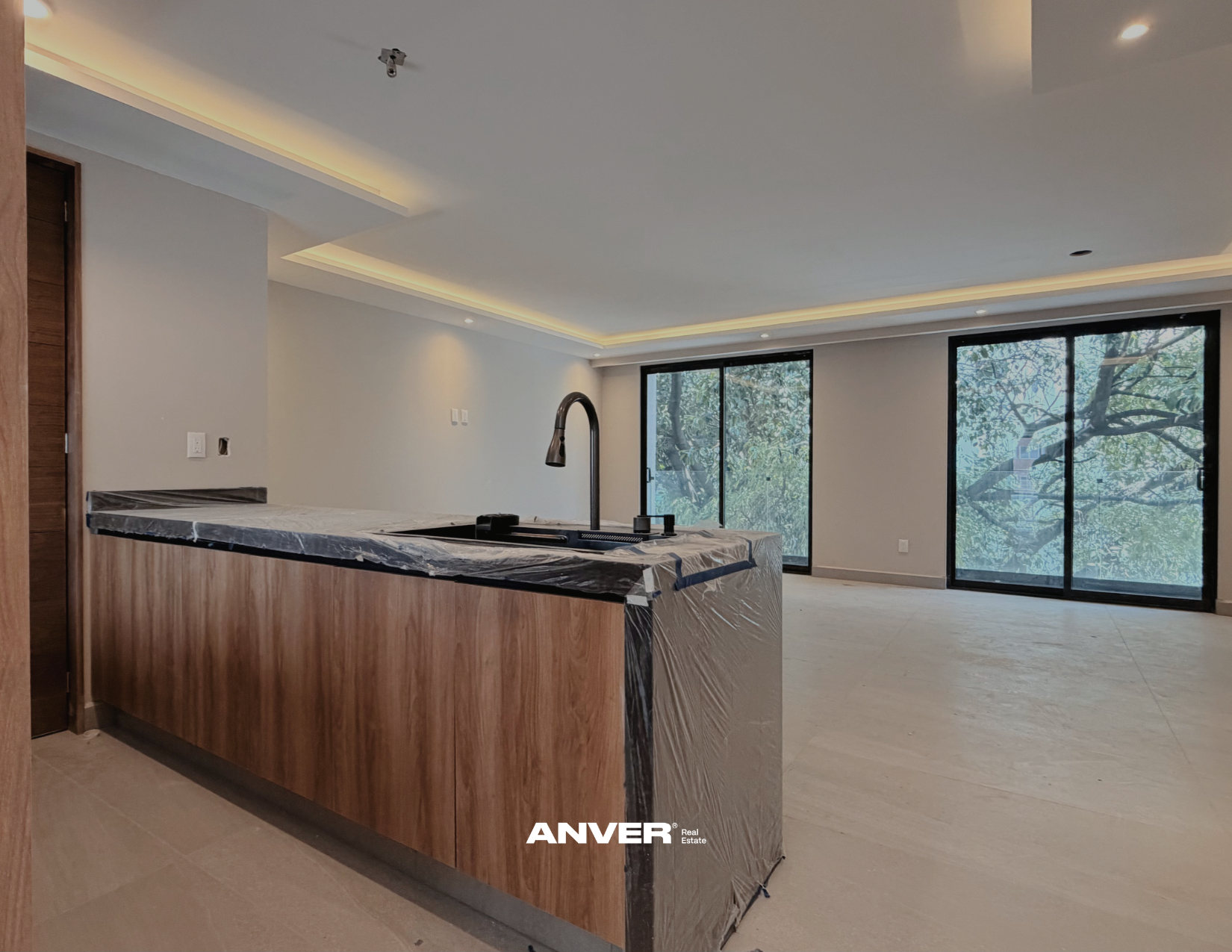Interiores de una sala moderna aún en construcción, con ventanas grandes y una barra de cocina de madera con encimera de mármol.