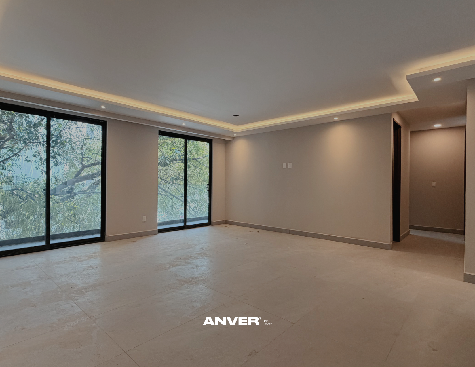 Espacio vacío en una sala moderna con ventanas de vidrio y puertas corredizas, paredes blancas y techo con iluminación empotrada.