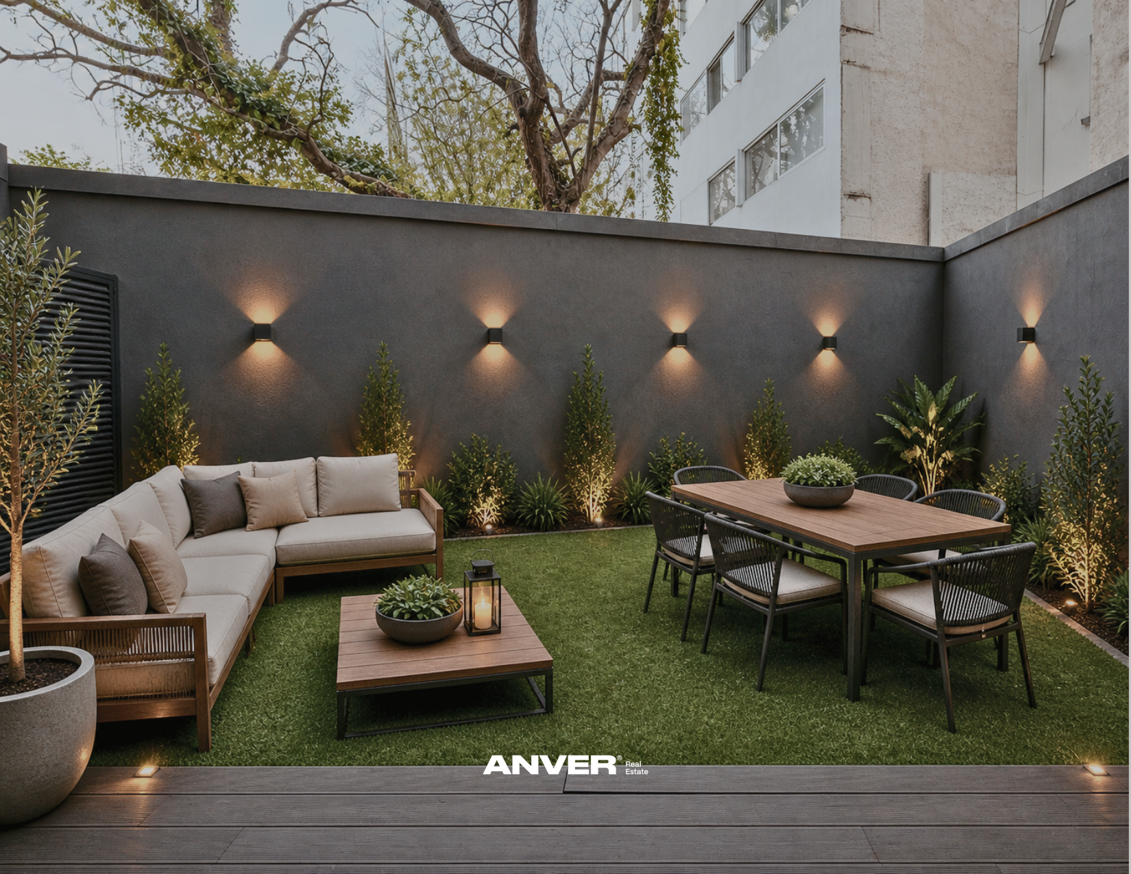 Un patio trasero con césped artificial, sofá con cojines, mesa de centro con plantas, mesa de comedor con sillas, iluminación en las paredes y plantas decorativas.