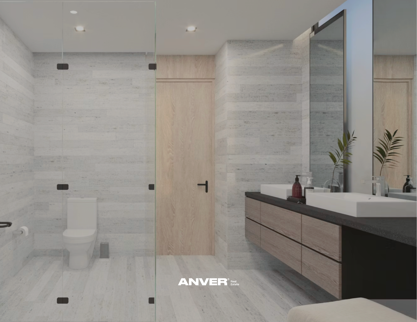 Interior de baño moderno con lavabo doble, espejo grande y plantas decorativas, paredes y suelo de piedra clara, puerta de madera y espejos en las paredes.