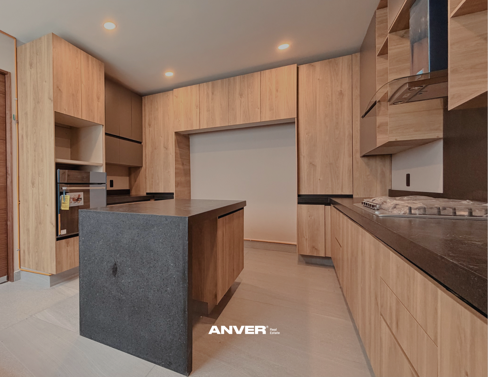 Cocina moderna con gabinetes de madera clara, islote de granito gris y estufa de gas