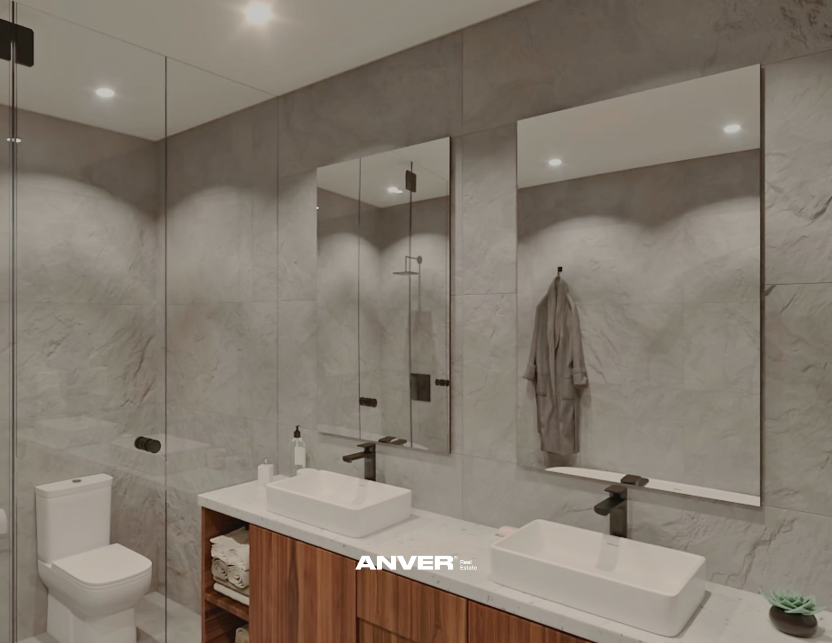Baño moderno con paredes de mármol, espejo grande sobre lavabo de madera, toallas en un estante y paredes de vidrio que muestran ducha con lluvia portátil, en el fondo hay inodoro, dispensador de jabón y adornos.