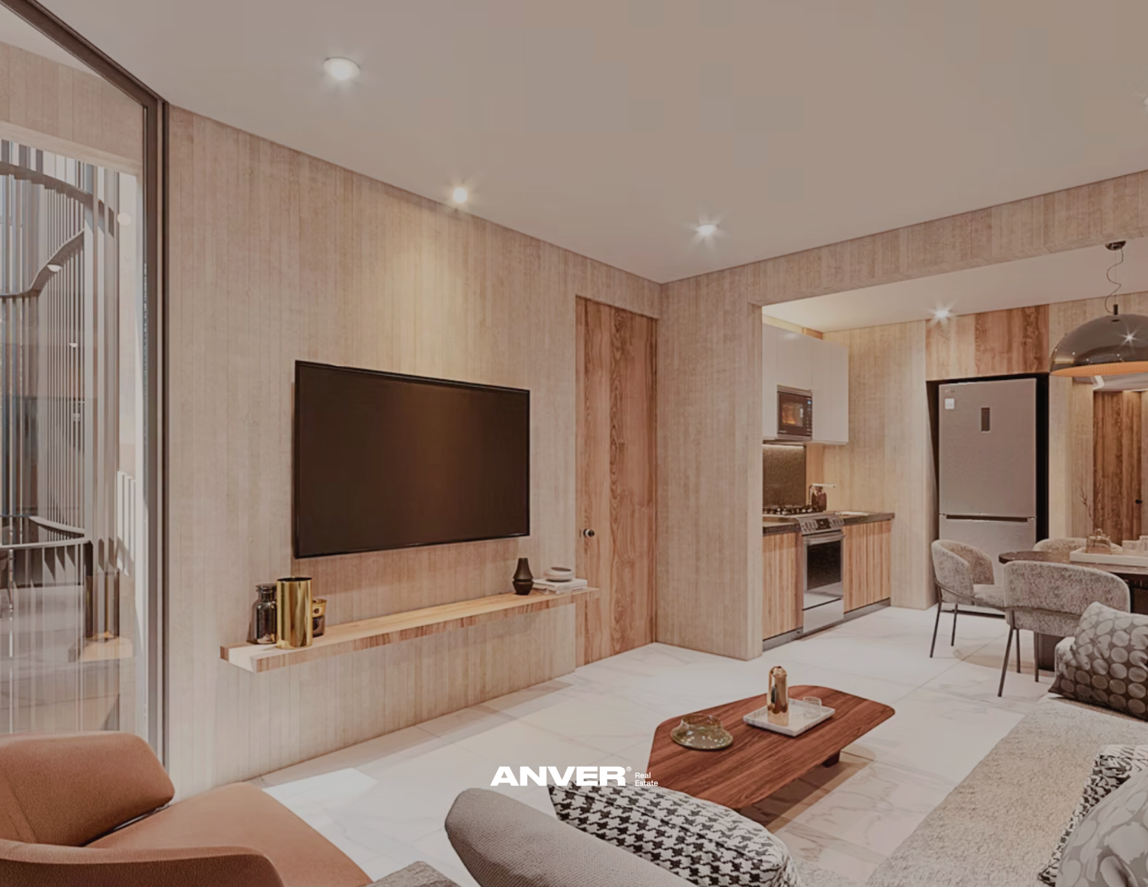 Sala de estar moderna con televisor montado en pared de madera clara, muebles decorativos y área de cocina con electrodomésticos en tonos de madera y gris, sillones y mesa de centro. 