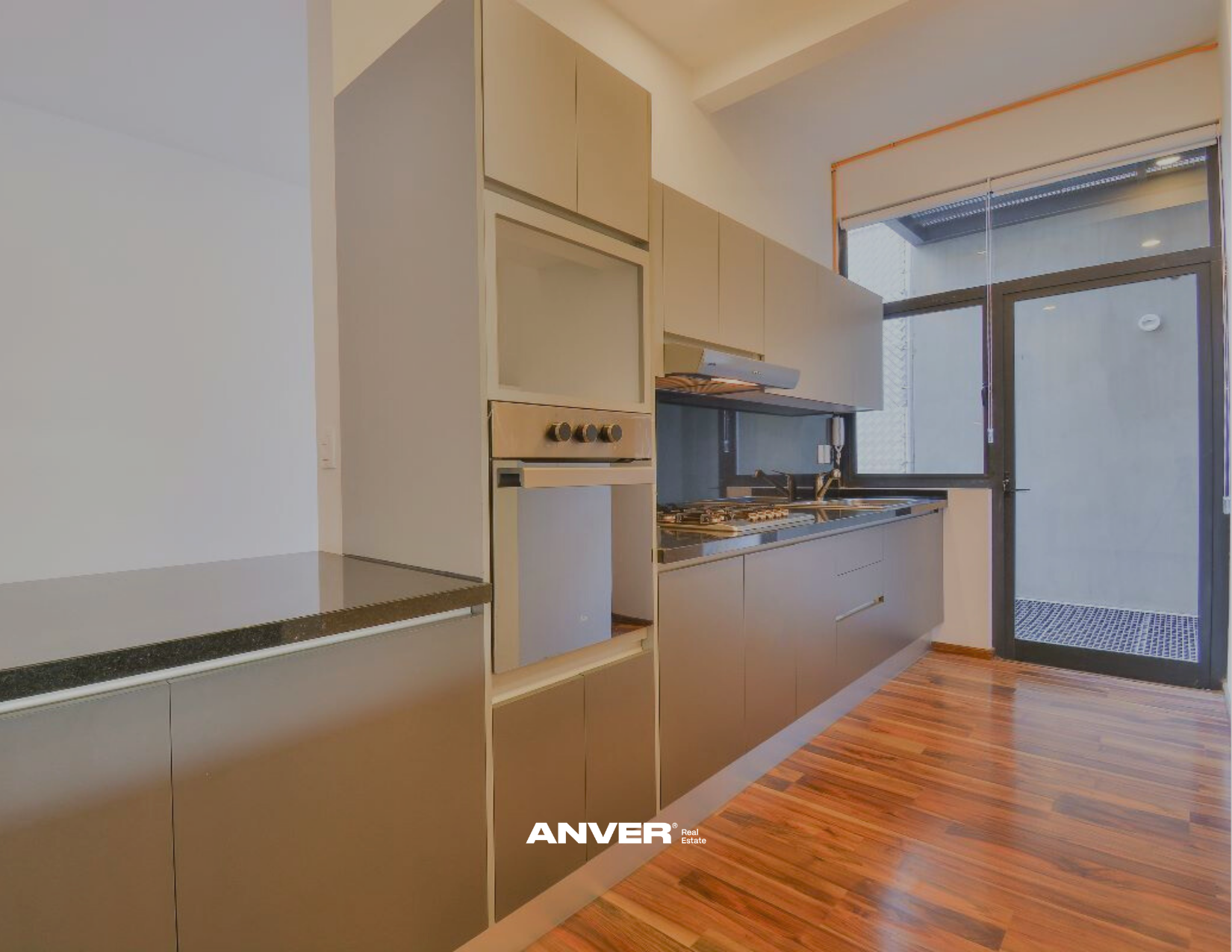 Cocina moderna con gabinetes beige y una ventana grande con persiana. Estufa y fregadero en la encimera. Piso de madera.
