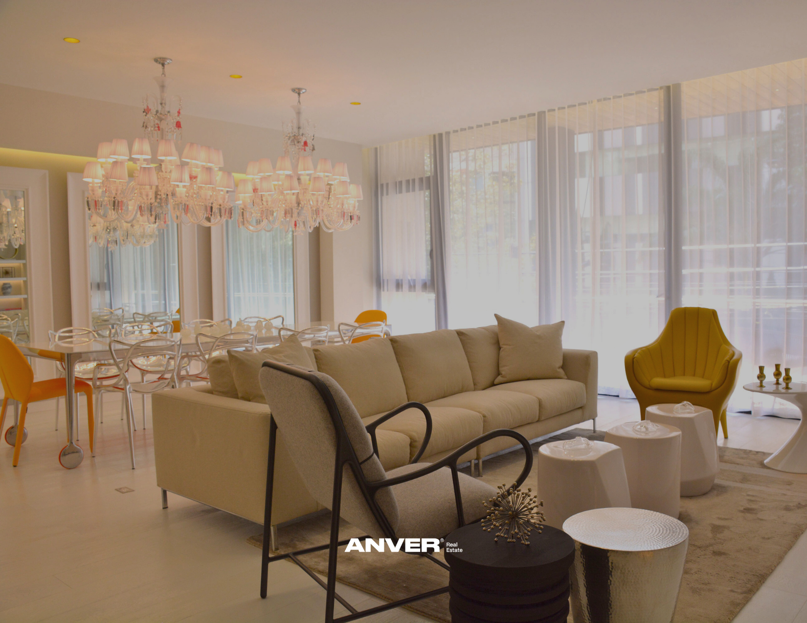 Sala moderna con cortinas blancas, sillones beige, sillas blancas y naranjas, lámparas de araña y buen iluminado natural.