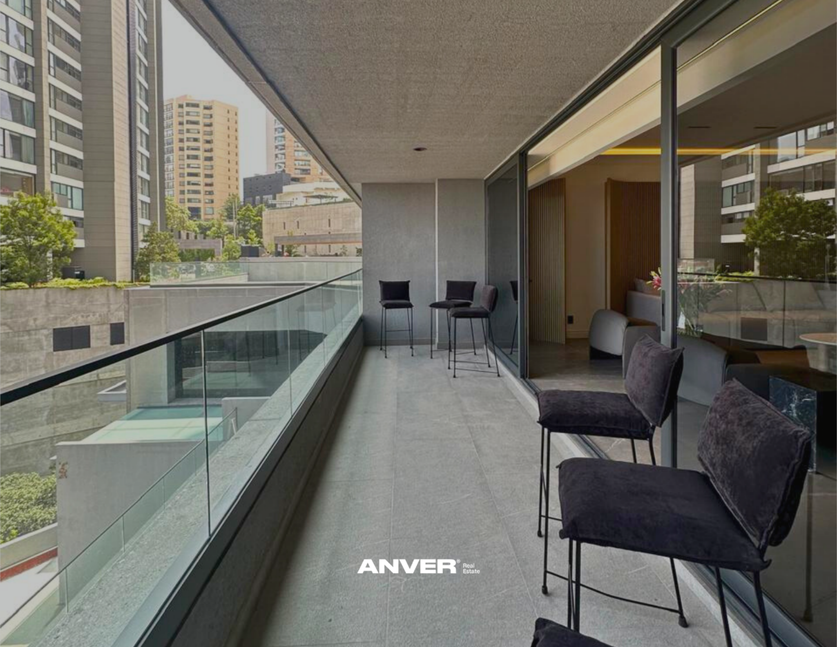 Balconera con sillas negras y mesa, vista de edificios urbanos con árboles, interior con sillones y decoración moderna.