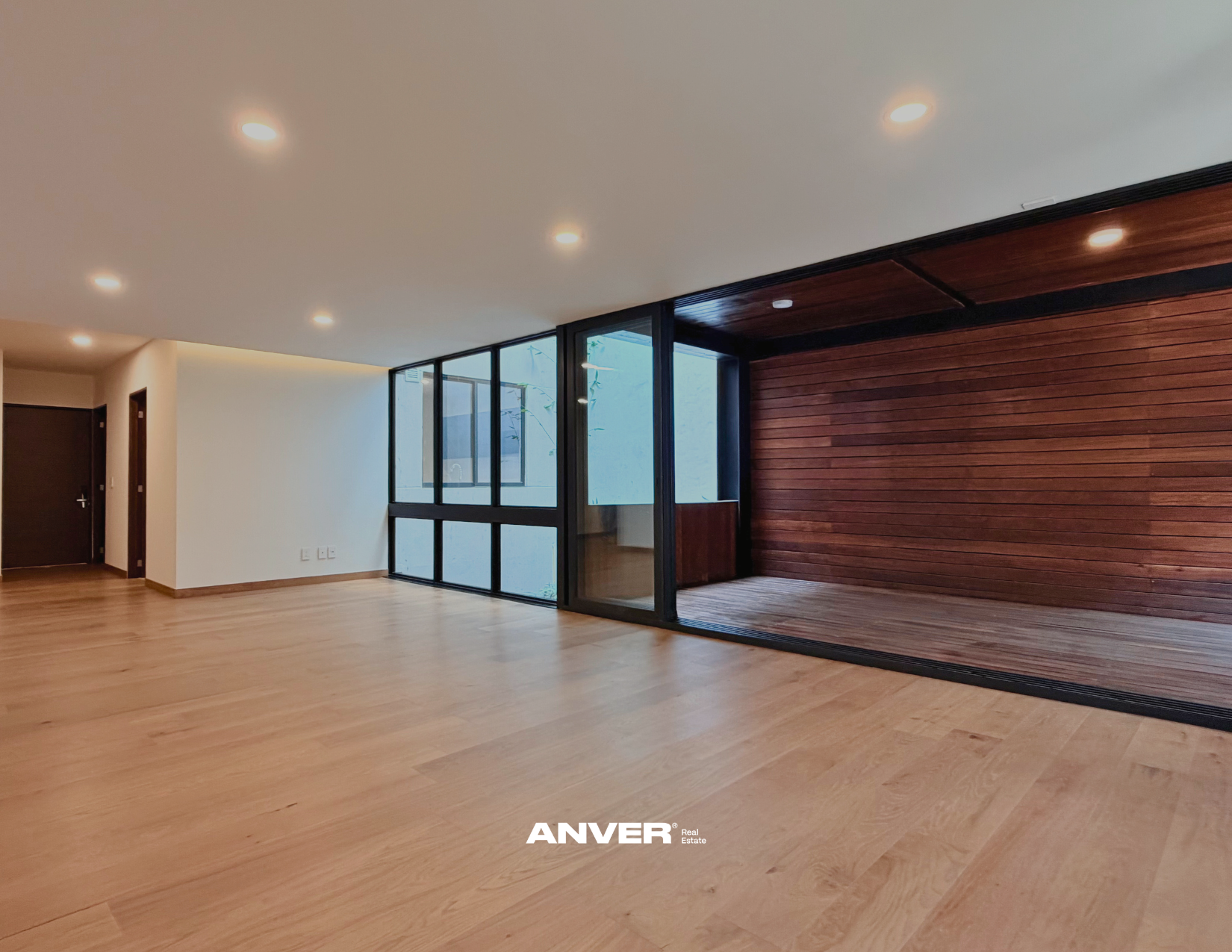 Interiores de una sala moderna con paredes blancas y una pared de madera, piso de madera y ventanas de vidrio con marco negro, iluminación empotrada en el techo
