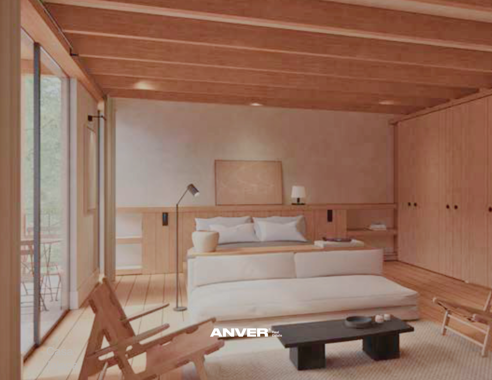 Sala de estar con paredes y techo de madera, cama con almohadas blancas, lámpara de lectura y mesa de noche, vista exterior a través de ventanas y balcón con sillas de madera.