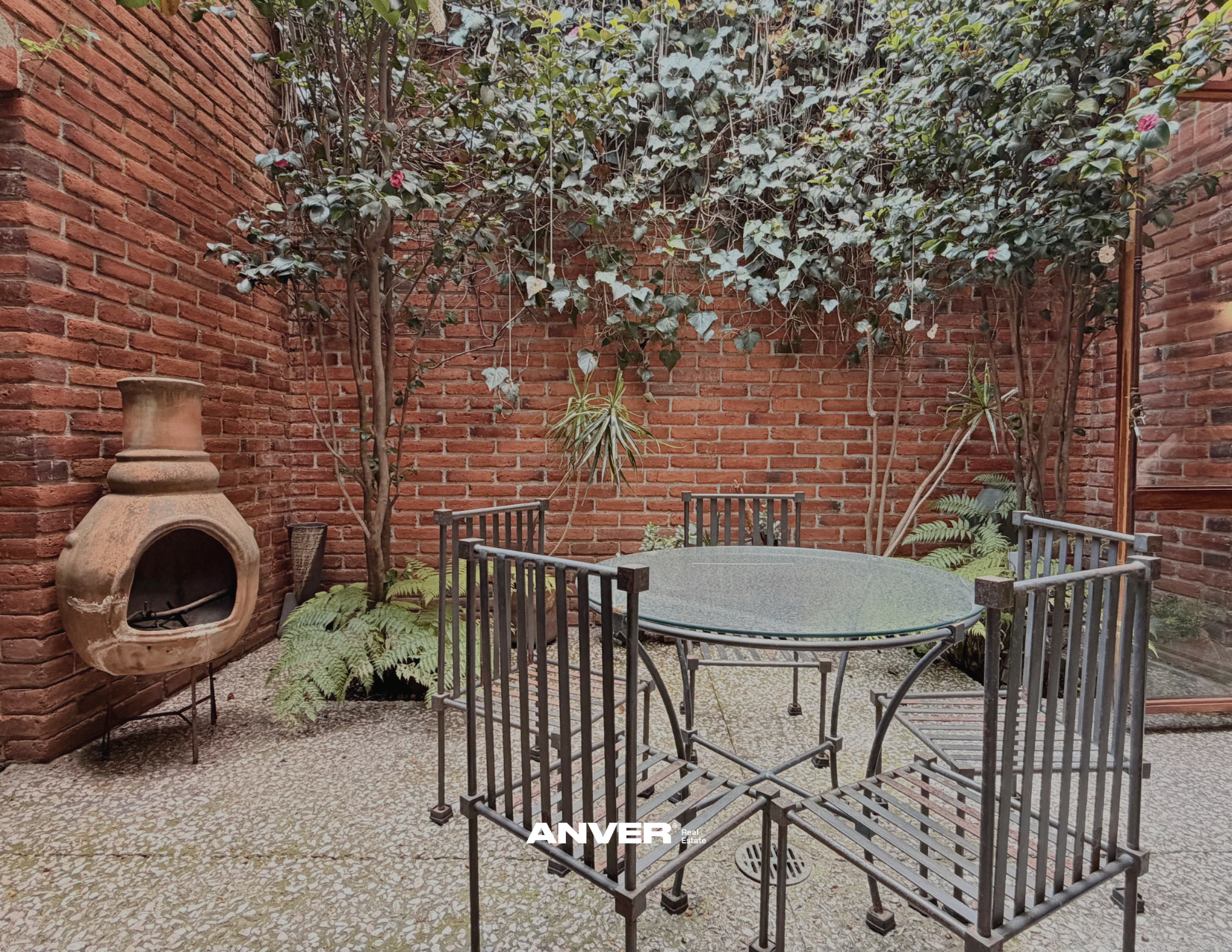 Patio con muebles de metal, plantas y paredes de ladrillo.