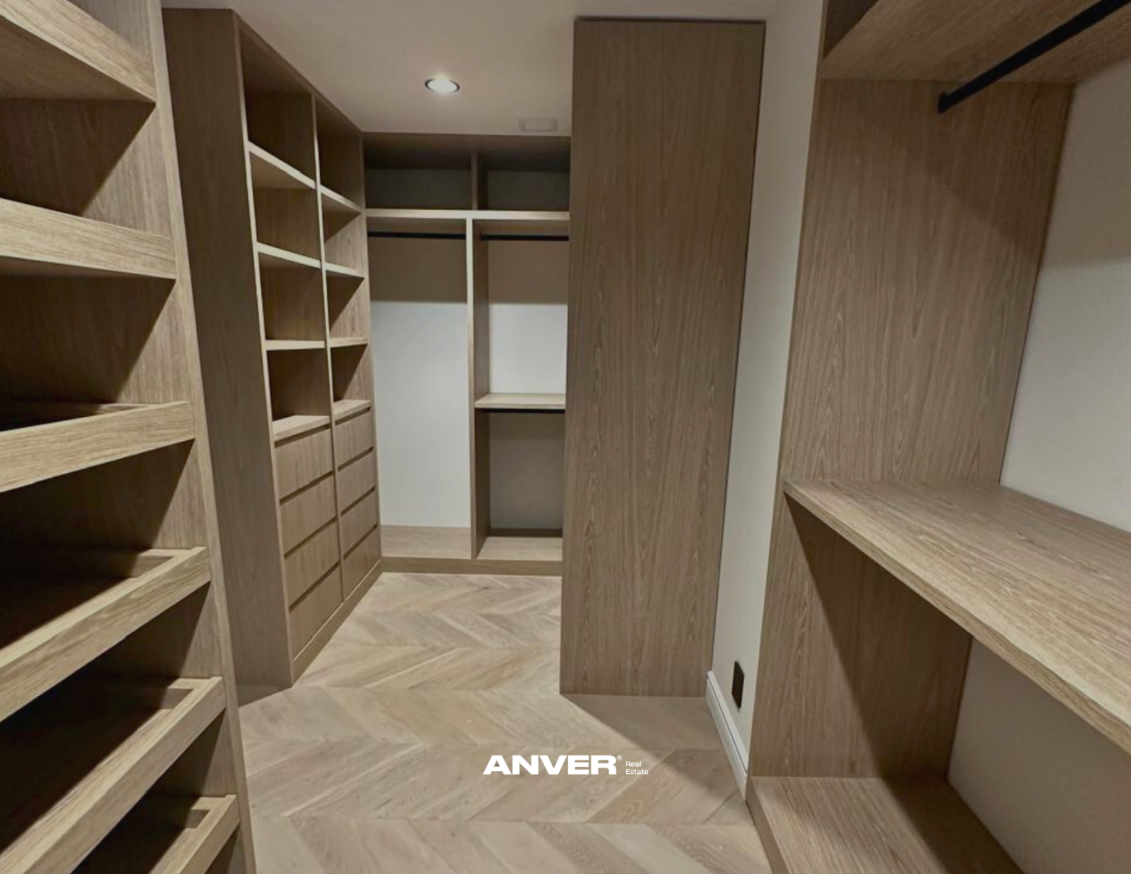 Armario de madera con estantes y compartimentos en un vestidor con piso de madera y luz empotrada en el techo.