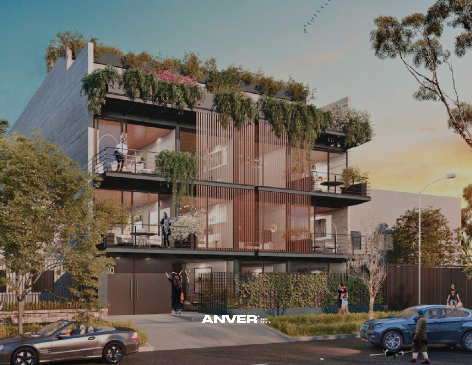 Edificio moderno de múltiples pisos con balcones y áreas verdes en la azotea, durante la puesta del sol, rodeado de árboles y calles con autos y peatones.