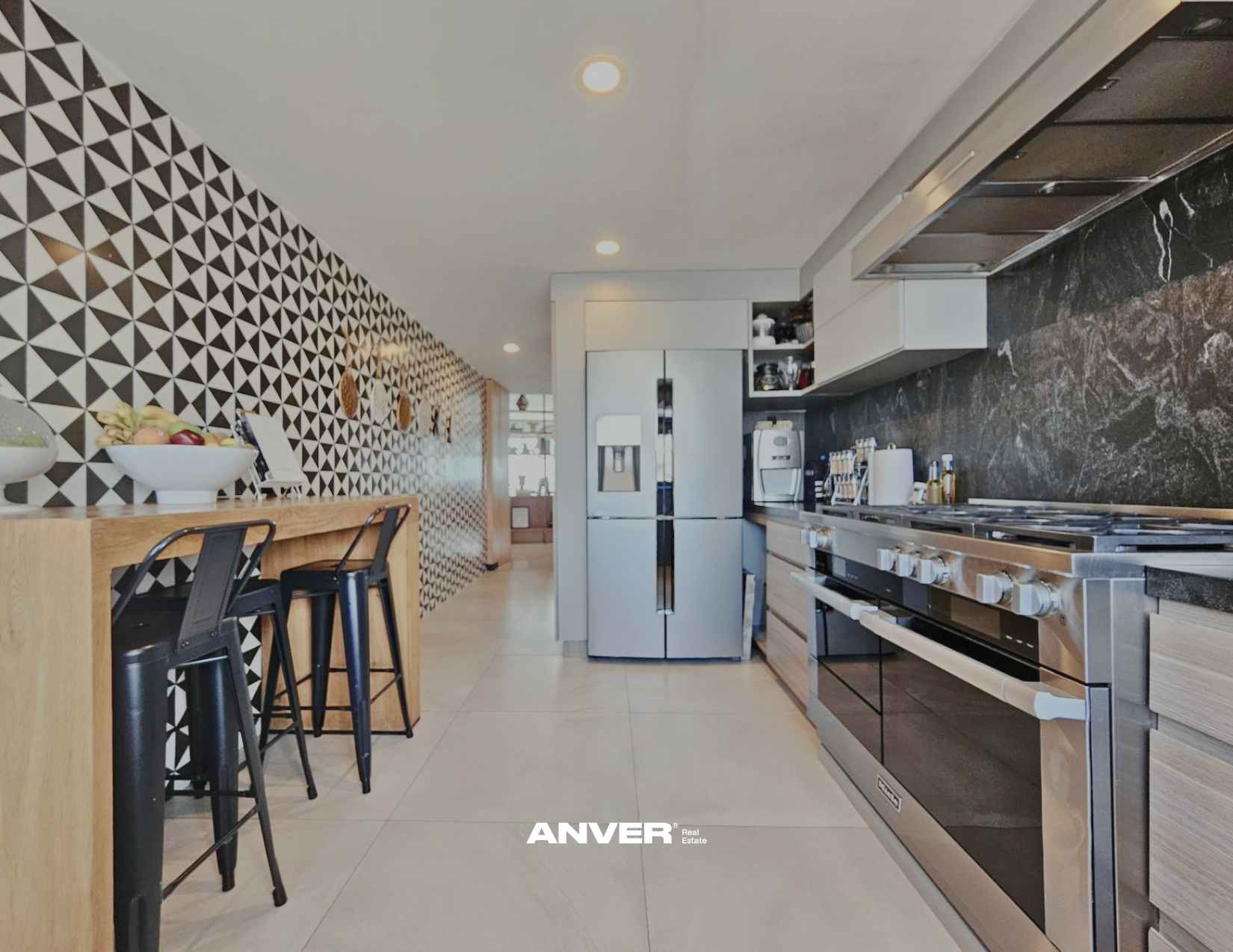 Cocina moderna con electrodomésticos de acero inoxidable y pared decorativa con patrón geométrico en tonos negros, blancos y grises.