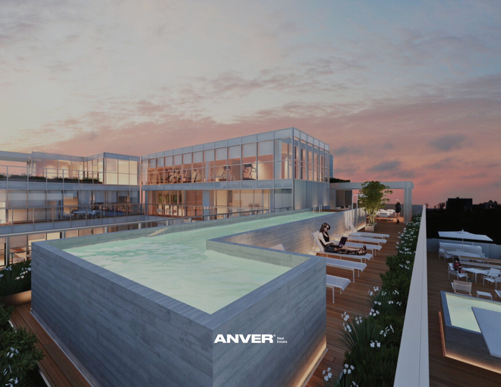 Vista nocturna de un edificio moderno con una piscina en la azotea, con personas relajándose y trabajando en sillones y haciendo ejercicio en un gimnasio visible en el interior, bajo un cielo con nubes y luz de atardecer.