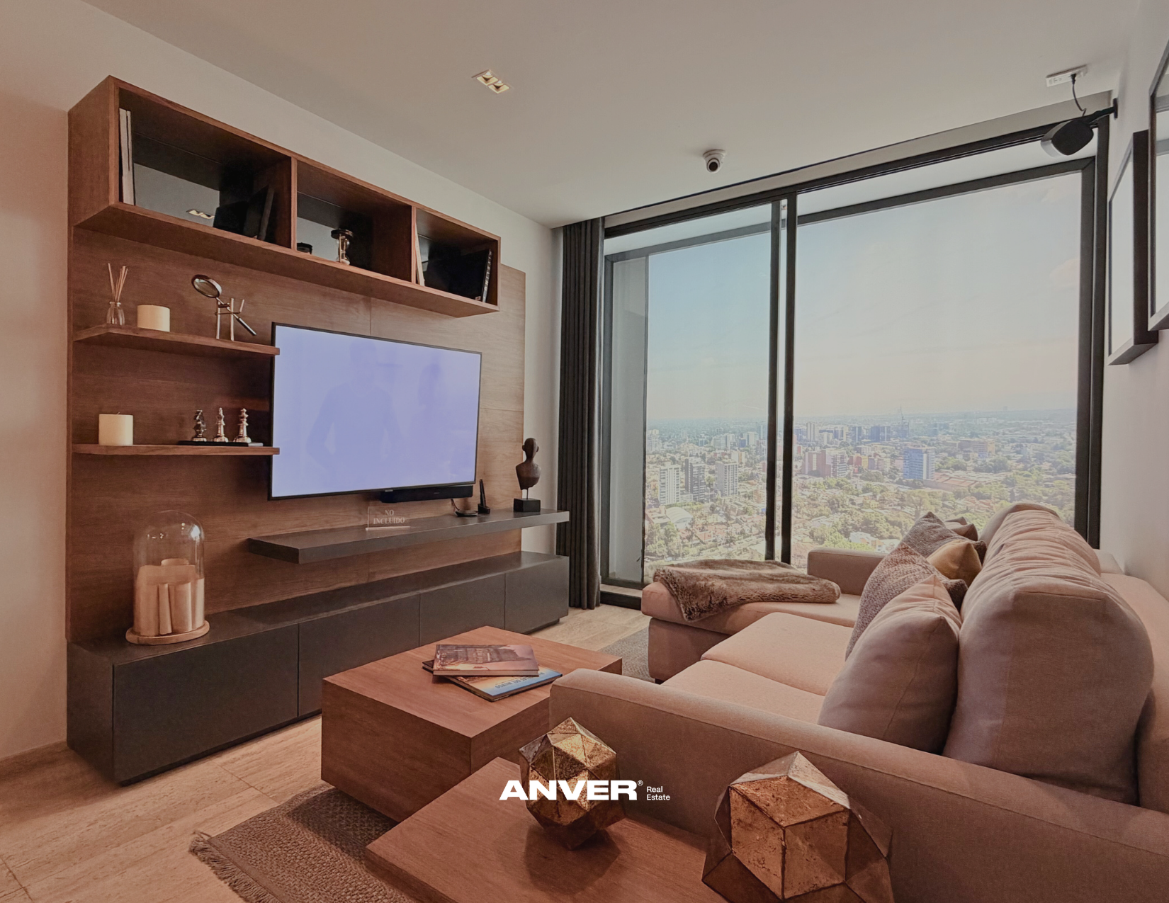 Sala moderna con televisor, sillón beige con cojines, mesa de centro de madera, vista panorámica de la ciudad por ventanales grandes, decoración minimalista con objetos de madera y velas.