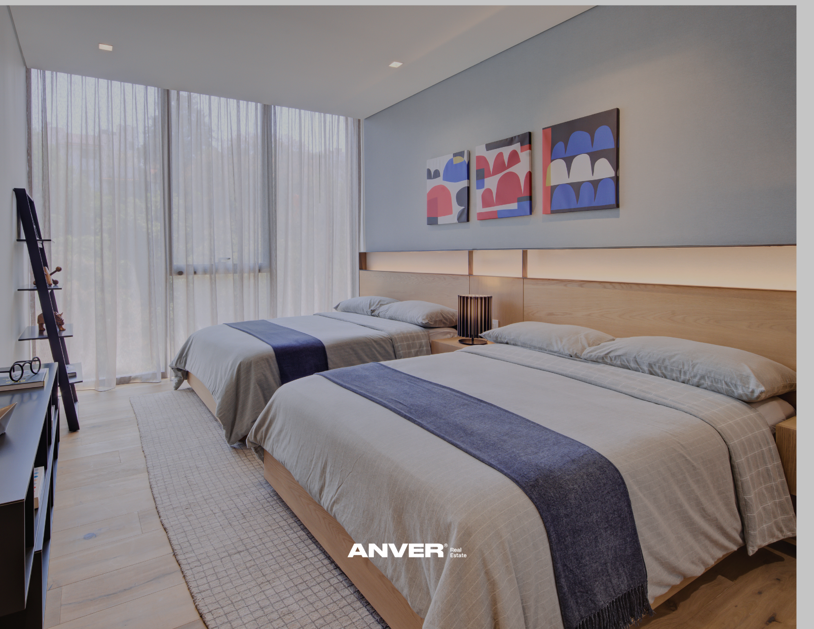 Dos camas en una habitación moderna con cortinas blancas y arte abstracto en la pared, incluyendo una lámpara sobre la mesa de noche y una repisa con objetos decorativos.
