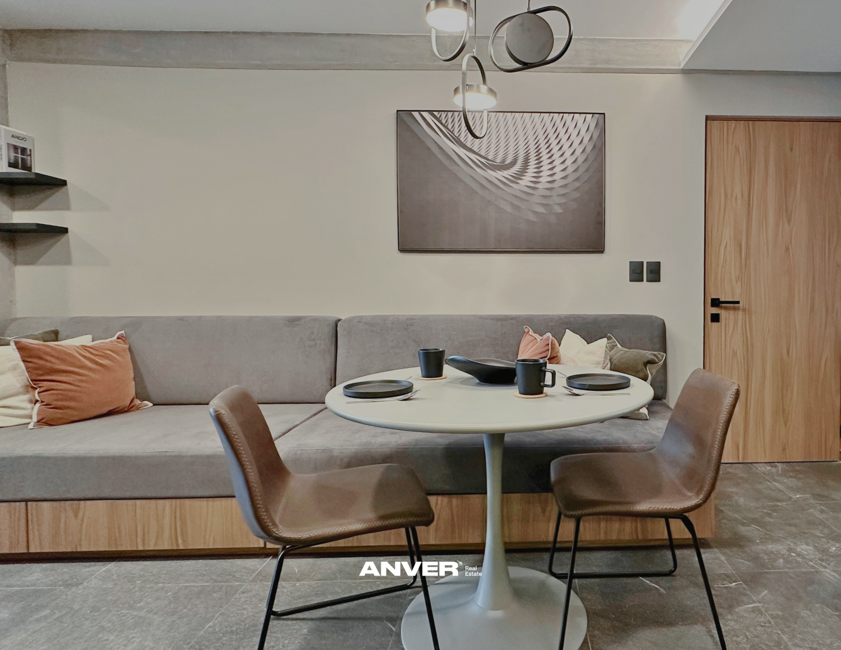 Sala de estar moderna con sofá gris, mesa redonda blanca, sillas de cuero marrón, cuadros decorativos y lámpara en el techo.