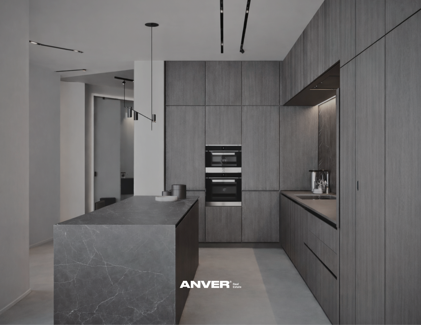 Cocina moderna con gabinetes de madera gris y una isla de mármol gris oscuro. Incluye horno empotrado, fregadero y gabinetes de pared, con iluminación minimalista. Marca: ANVER