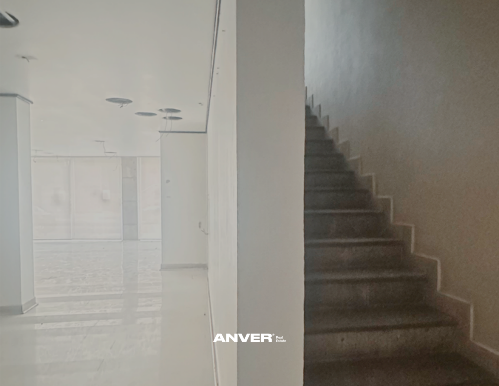 Vista del interior de un edificio en construcción o en proceso de remodelación, con paredes blancas, suelos de mármol y escaleras de madera. Se observa un espacio amplio y vacío con acabados en progreso.