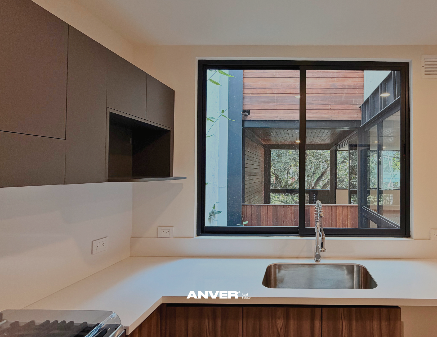 Vista desde una cocina con un fregadero, ventana grande y vista a un patio con paredes de madera y plantas.