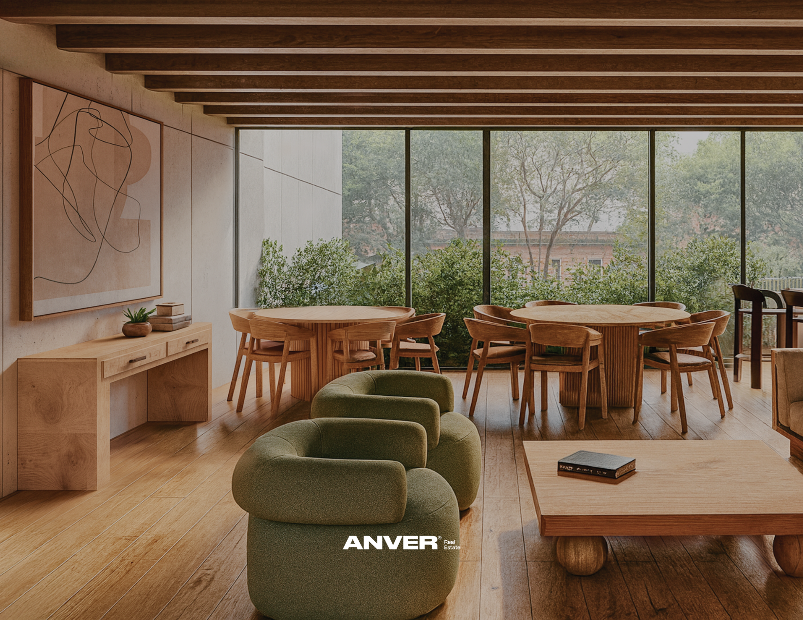 Interior de una sala con paredes de concreto y grandes ventanas con vista a árboles y plantas. Muebles de madera, incluyendo mesas redondas y sillas individuales. Sofás verdes y una mesa de centro de madera con un libro encima. Decoración minimalista con arte abstracto en la pared y una planta en una repisa.
