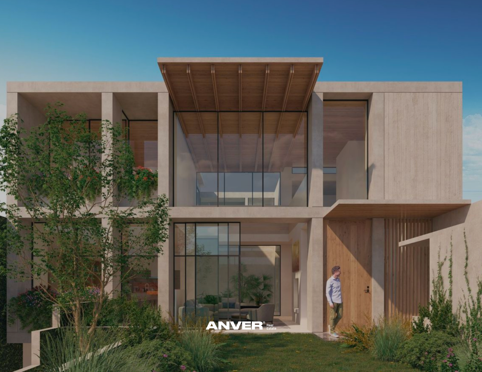 Vista frontal de una casa moderna de varios pisos con estructura en concreto y grandes ventanas de vidrio. Hay árboles y plantas en el jardín, una persona está de pie cerca de la entrada, bajo un cielo despejado.