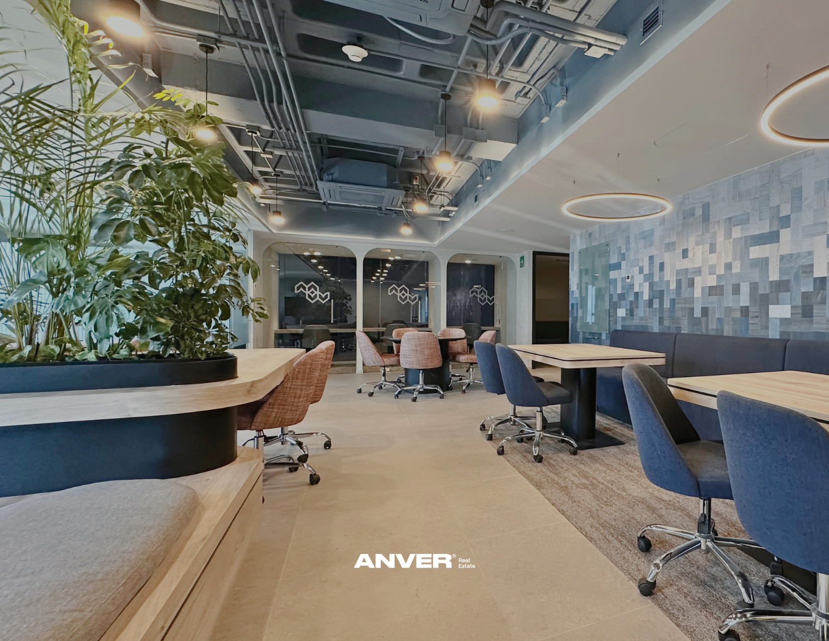 Interior moderno de oficina con mesas de madera, sillas de tela y plantas decorativas, iluminación lujosa y paredes con diseño geométrico.